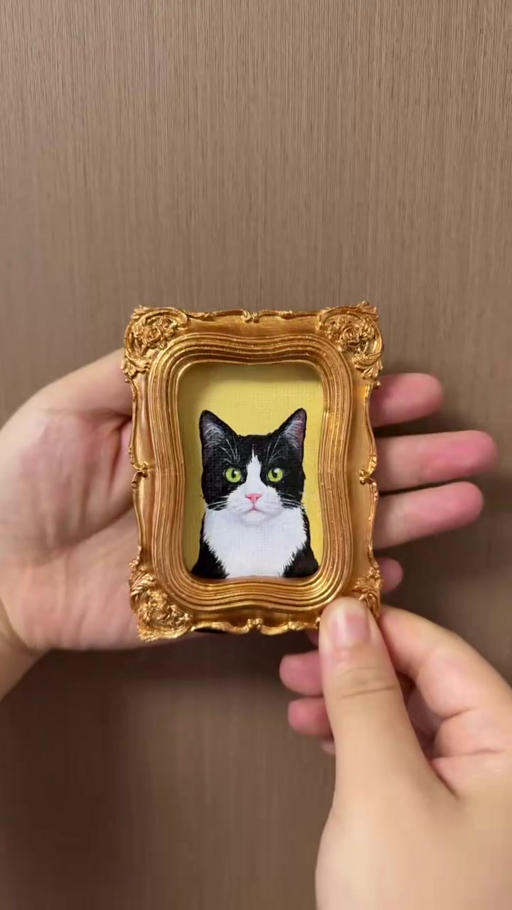 A small framed tuxedo cat oil portrait held in a hand
